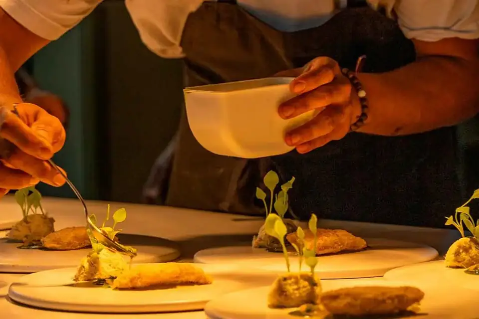 A chef's hands plating a row of dishes garnished with microgreens at the pass