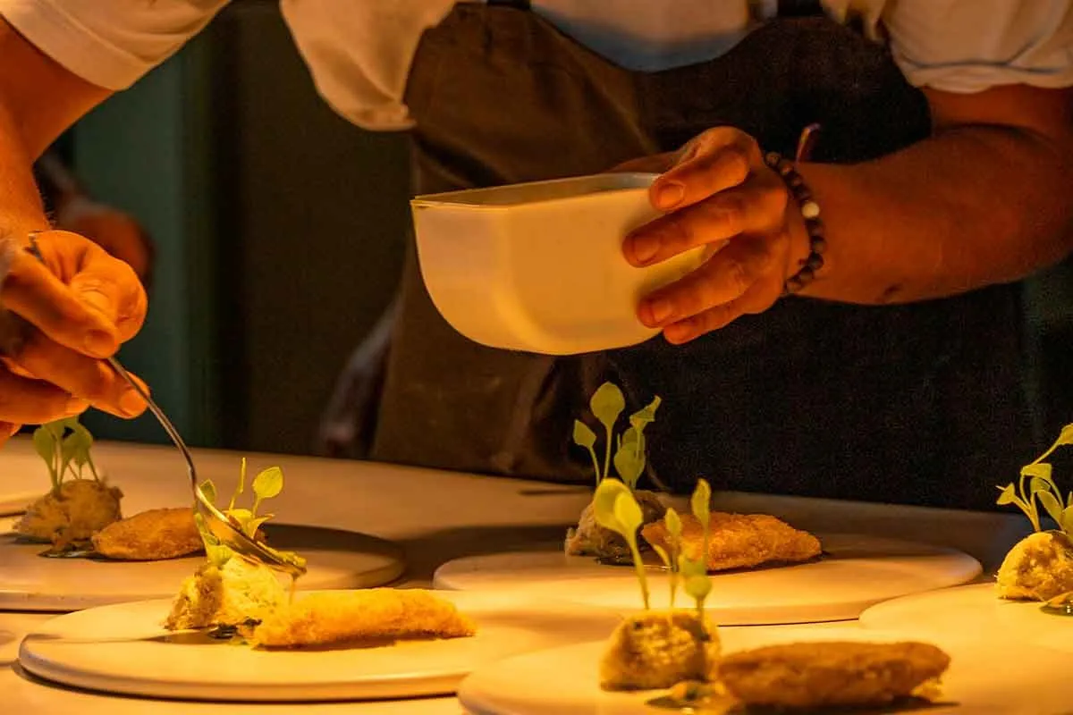A chef's hands plating a row of dishes garnished with microgreens at the pass