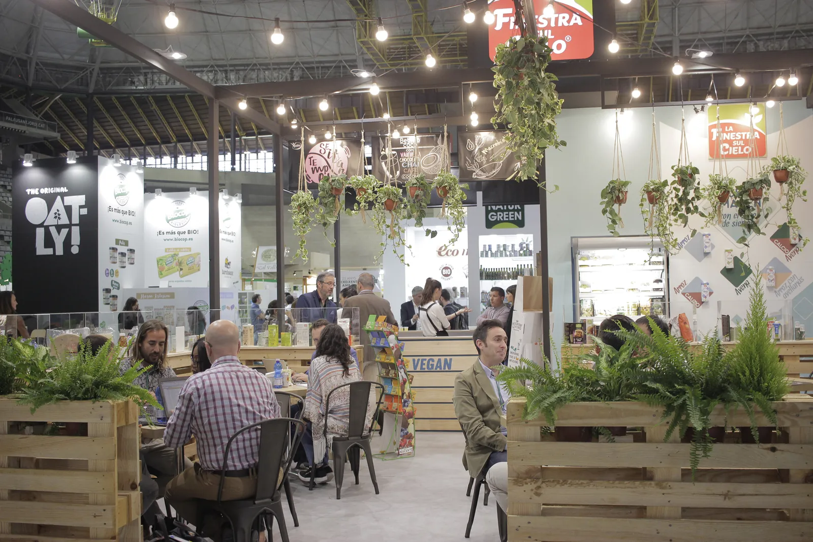 Exhibitor stands and a seating area with wooden planters inside a BioCultura fair hall