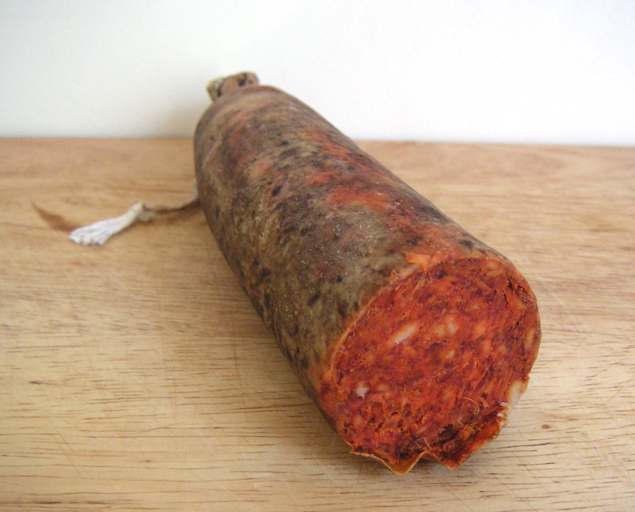 A cut sobrassada sausage on a wooden board showing its red pepper colored interior