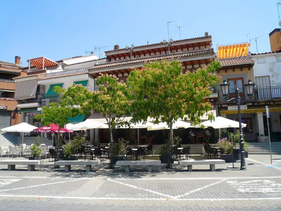 A town square in El Molar with trees, café umbrellas and two-storey buildings.