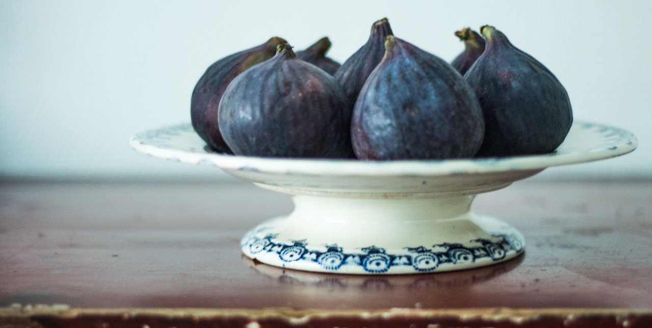 A pile of fresh purple figs on a decorative pedestal plate