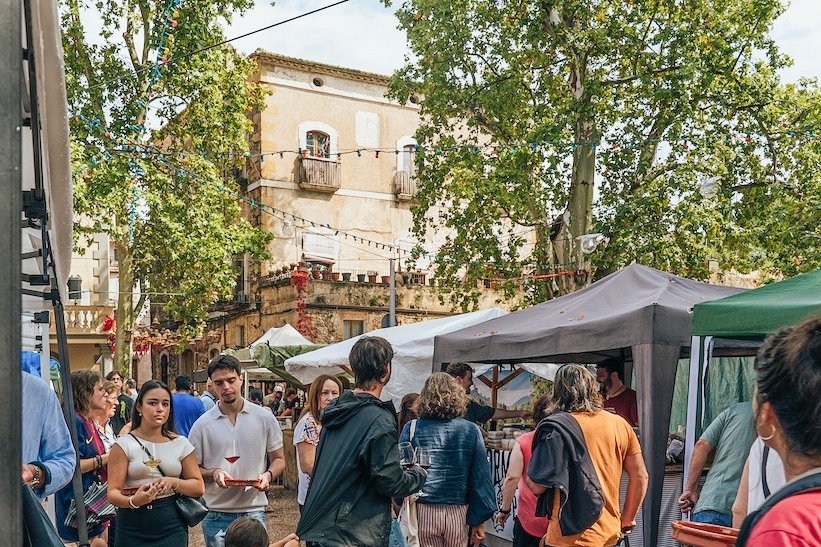 Crowd browsing market stalls under plane trees at the Lladó cheese fair