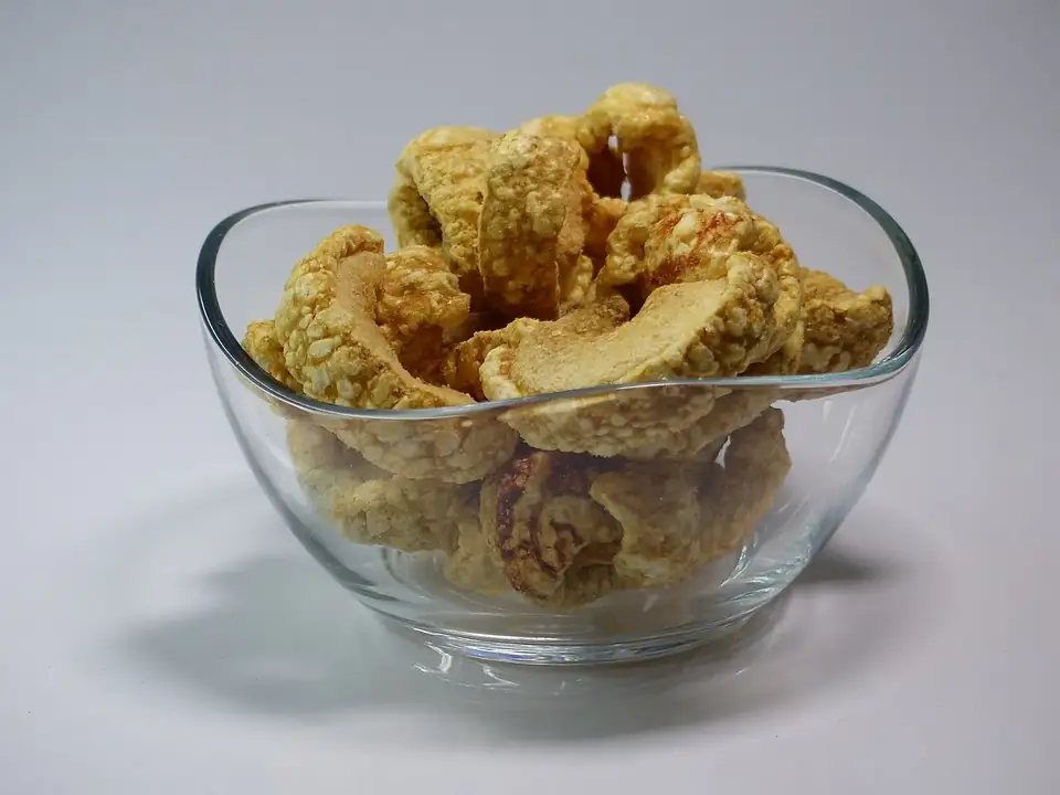 A glass bowl of crispy torreznos (fried pork belly) on a white background