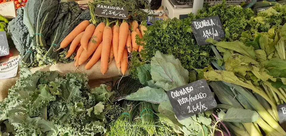 A market stall of fresh carrots, kale, escarole and kohlrabi with handwritten chalkboard price signs