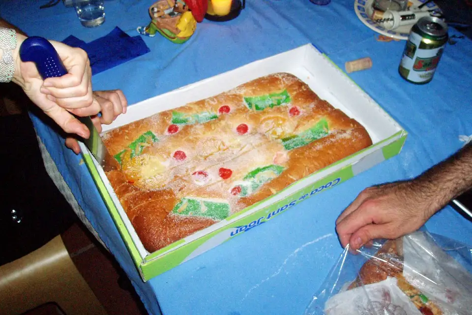 A coca de Sant Joan topped with candied fruit, being opened on a table