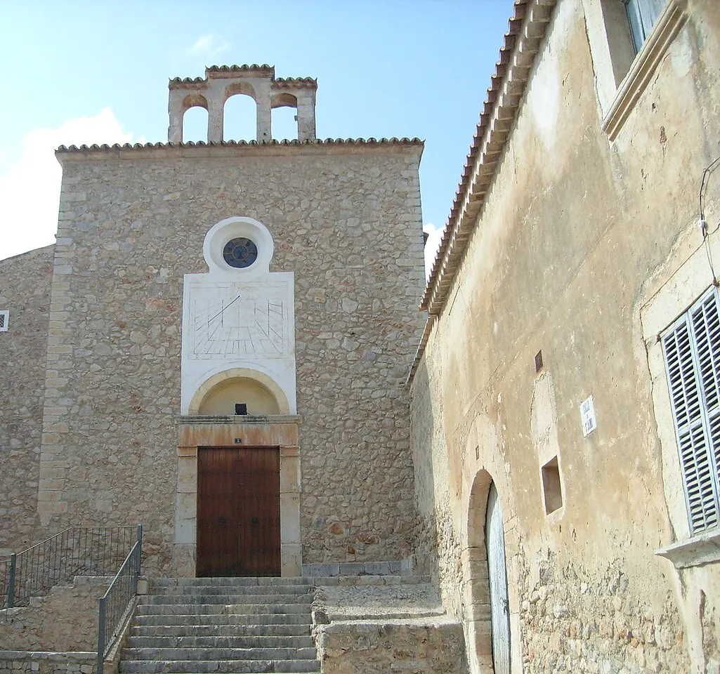 The stone façade and bell gable of the Església Vella in Caimari, with steps up to its wooden door