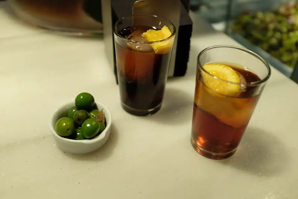Two glasses of vermouth with orange and a bowl of green olives