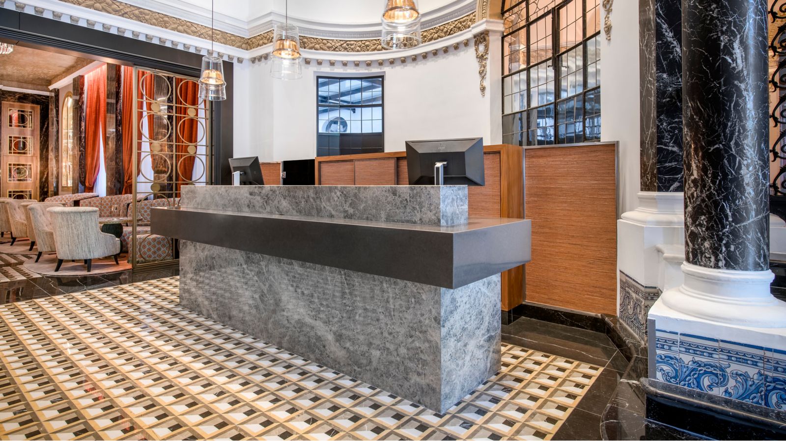 The reception: a grey marble front desk on a geometric tiled floor between black marble columns, under a gilded frieze, with a curtained lounge beyond.
