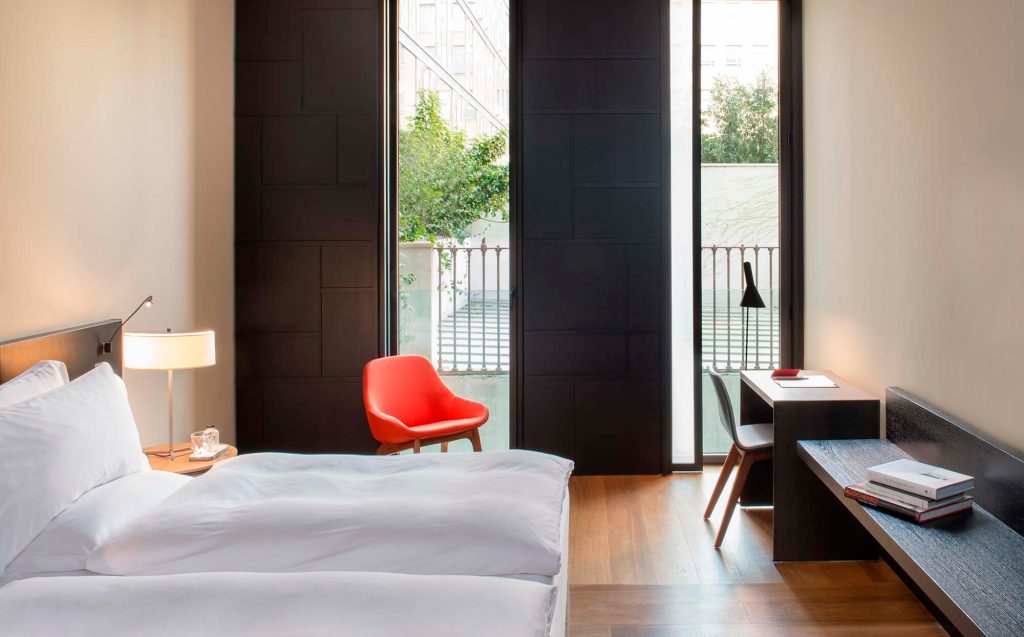 Deluxe room with white bedding, a red accent chair and a private balcony