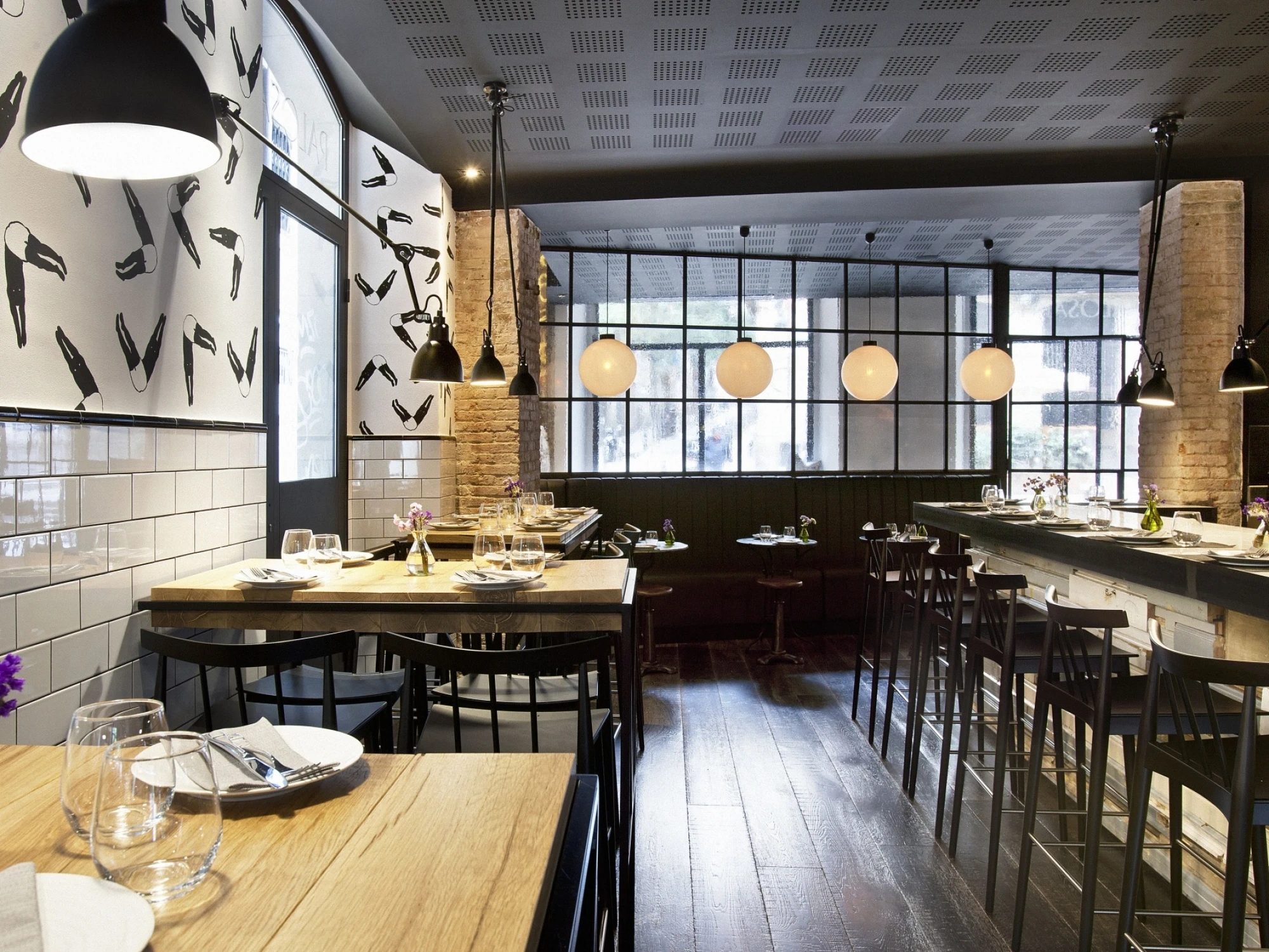Dining room of Palosanto restaurant inside Arai Aparthotel, with globe pendant lights, subway-tiled walls, and wood tables set for service