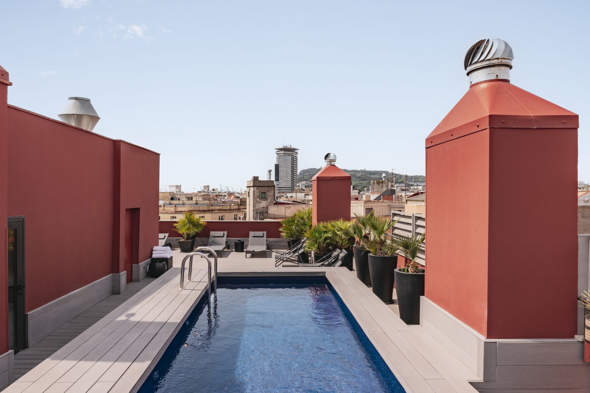 Rooftop plunge pool at Arai Aparthotel framed by terracotta chimney stacks with sun loungers and a view over Barcelona's rooftops