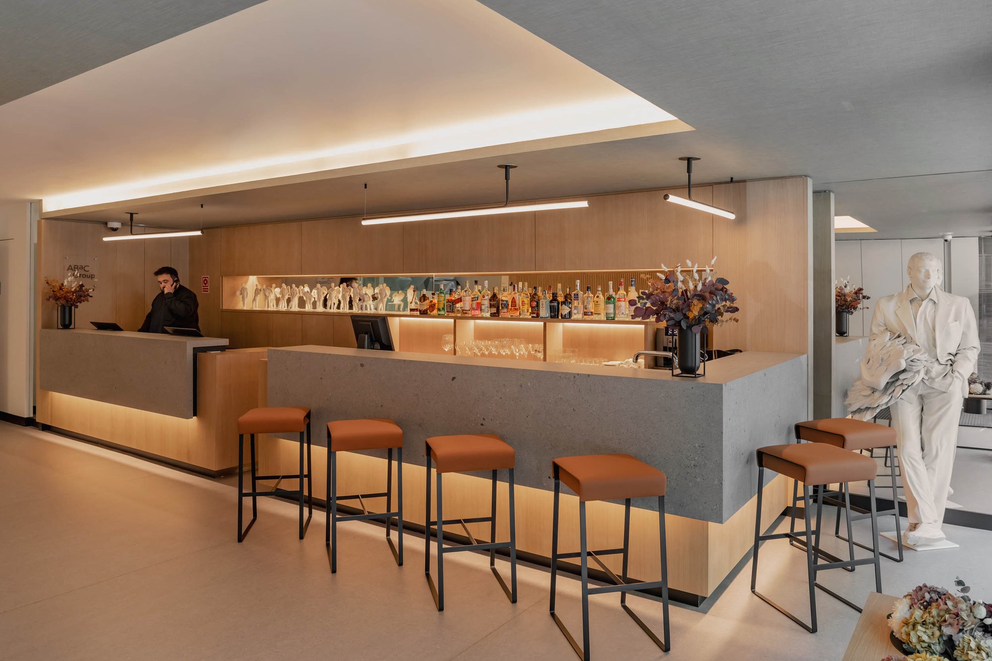 Bar at Hotel Arconte with a pale stone counter, orange stools and backlit shelves of bottles