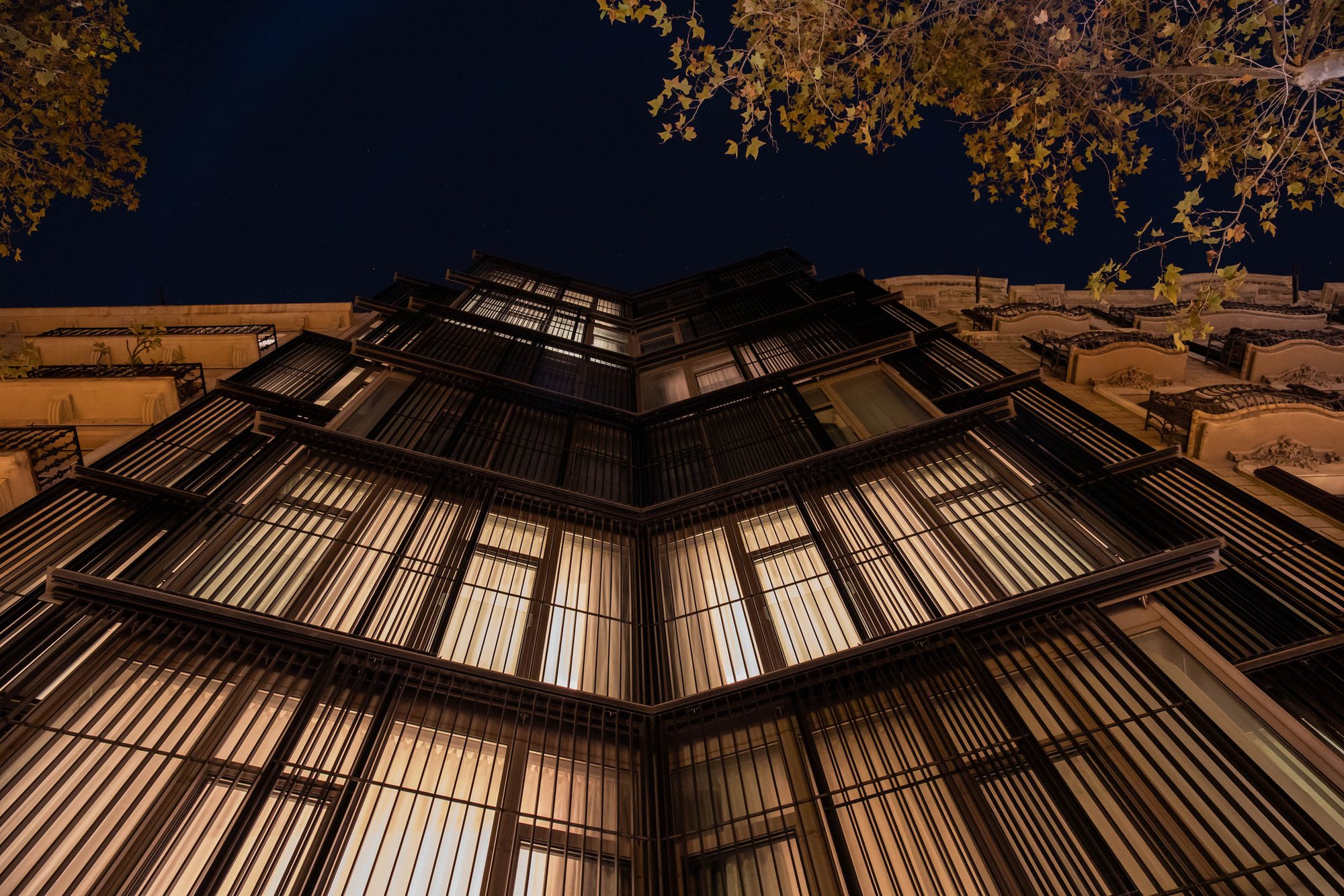 Hotel Arconte's geometric metal facade lit from within at night, seen from street level