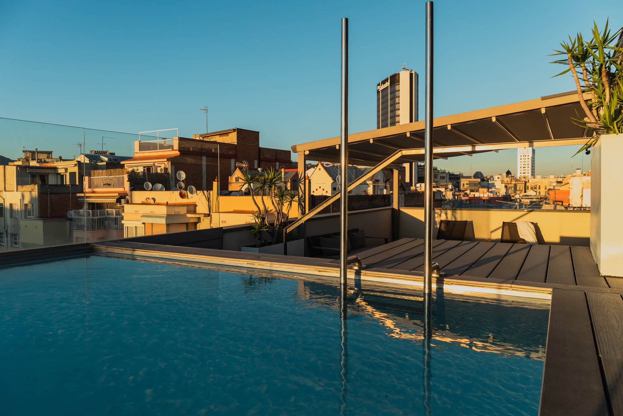 Pool terrace at Hotel Arconte with a long narrow pool, steel handrails and city rooftops under a clear sky