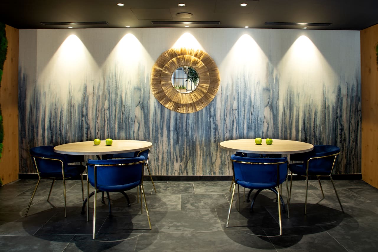 A dining area at Atocha 107 with round wooden tables, navy blue chairs and a decorative round mirror on a textured wall.