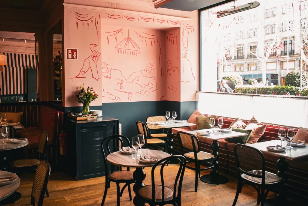 Batea's dining room, with bentwood chairs and marble-top tables in front of a pink mural of diners on the wall.