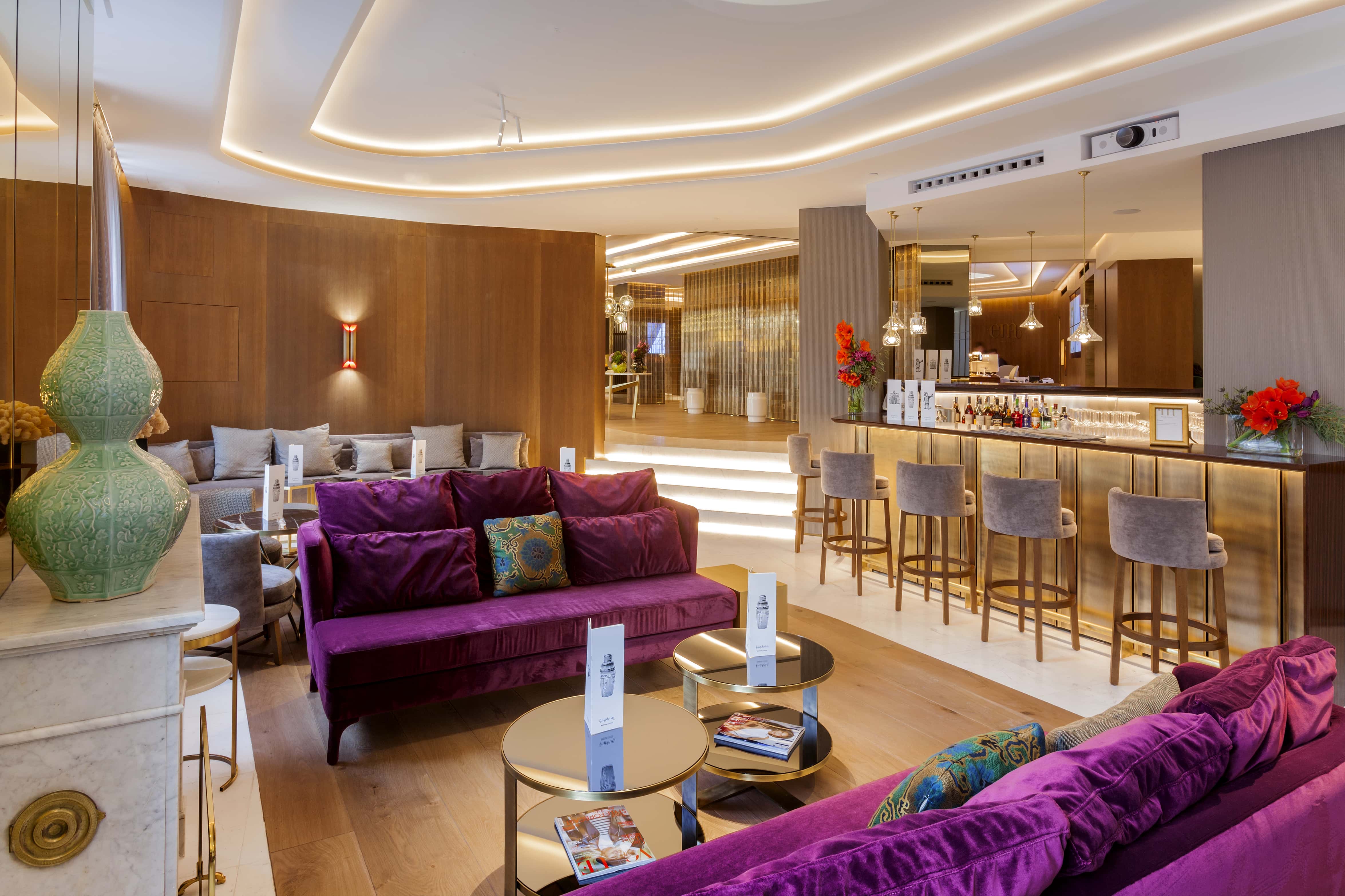 The bar at Barcelo Emperatriz: a brass-fronted counter lined with grey upholstered stools, with purple velvet sofas and low mirrored tables in the lounge in front of it.