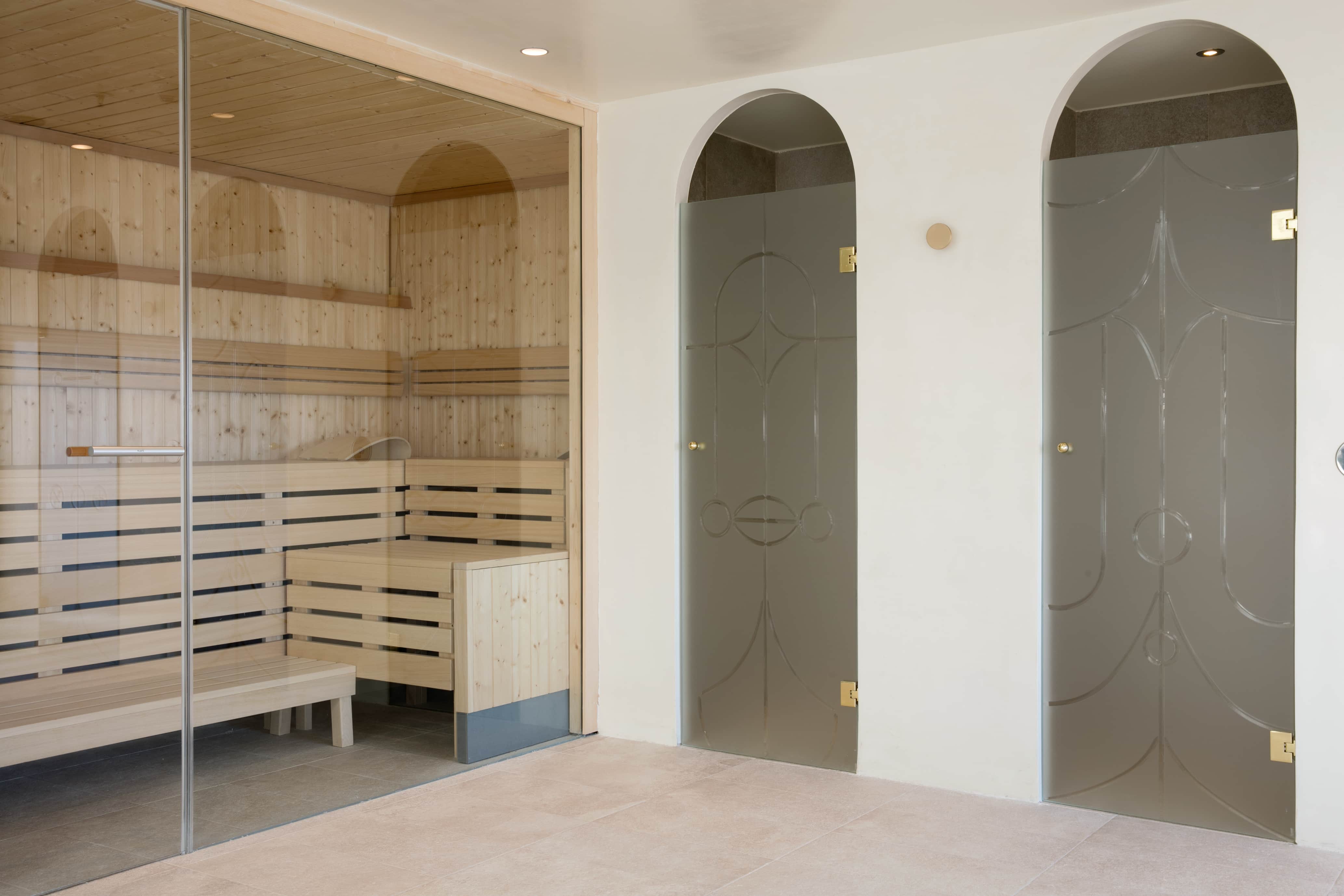 The spa at Barcelo Torre de Madrid: a glass-fronted wooden sauna with tiered benches, next to two arched grey doors set into a pale stone-tiled wall.