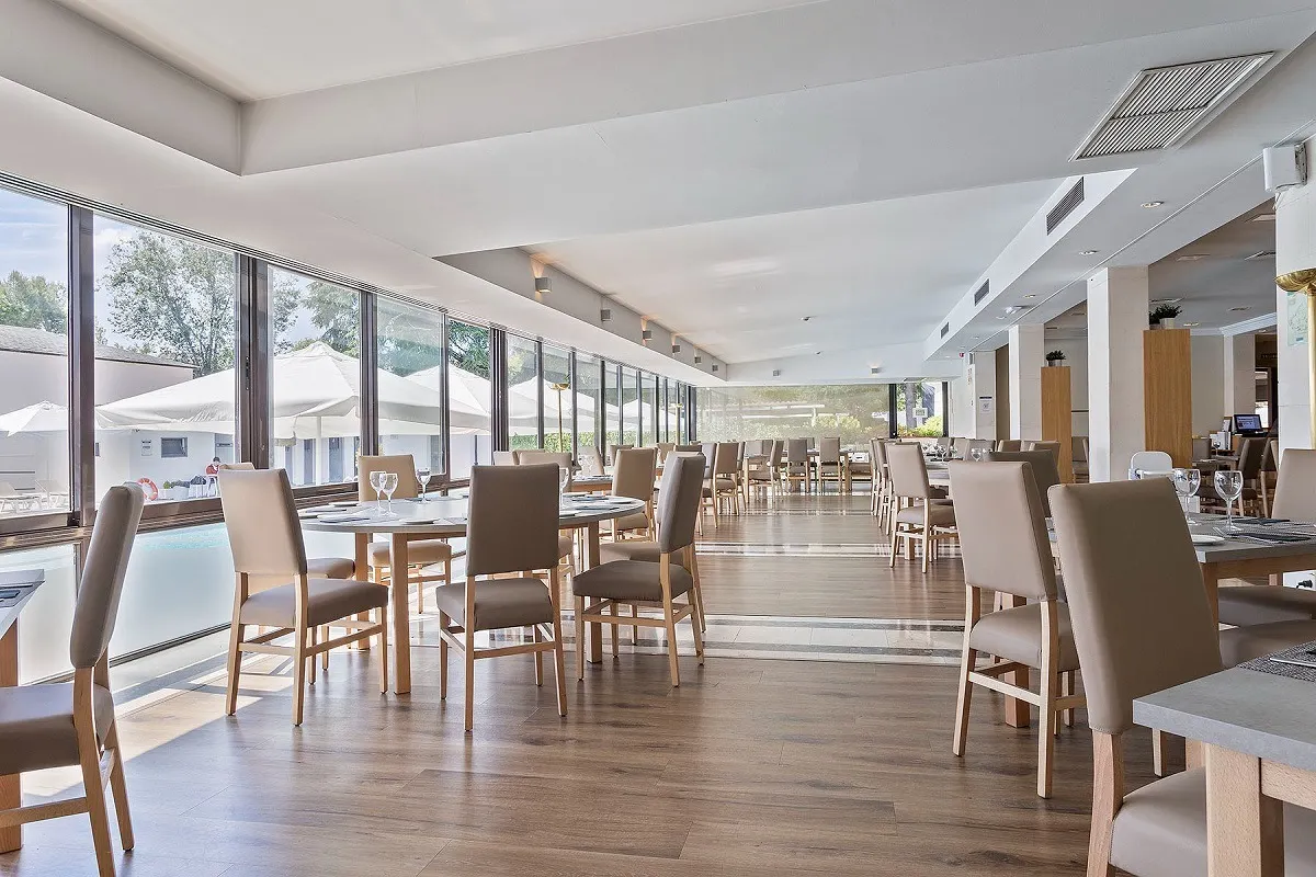 H2O Restaurant dining room with rows of set tables and beige chairs, floor-to-ceiling windows along one side looking out over the pool terrace.
