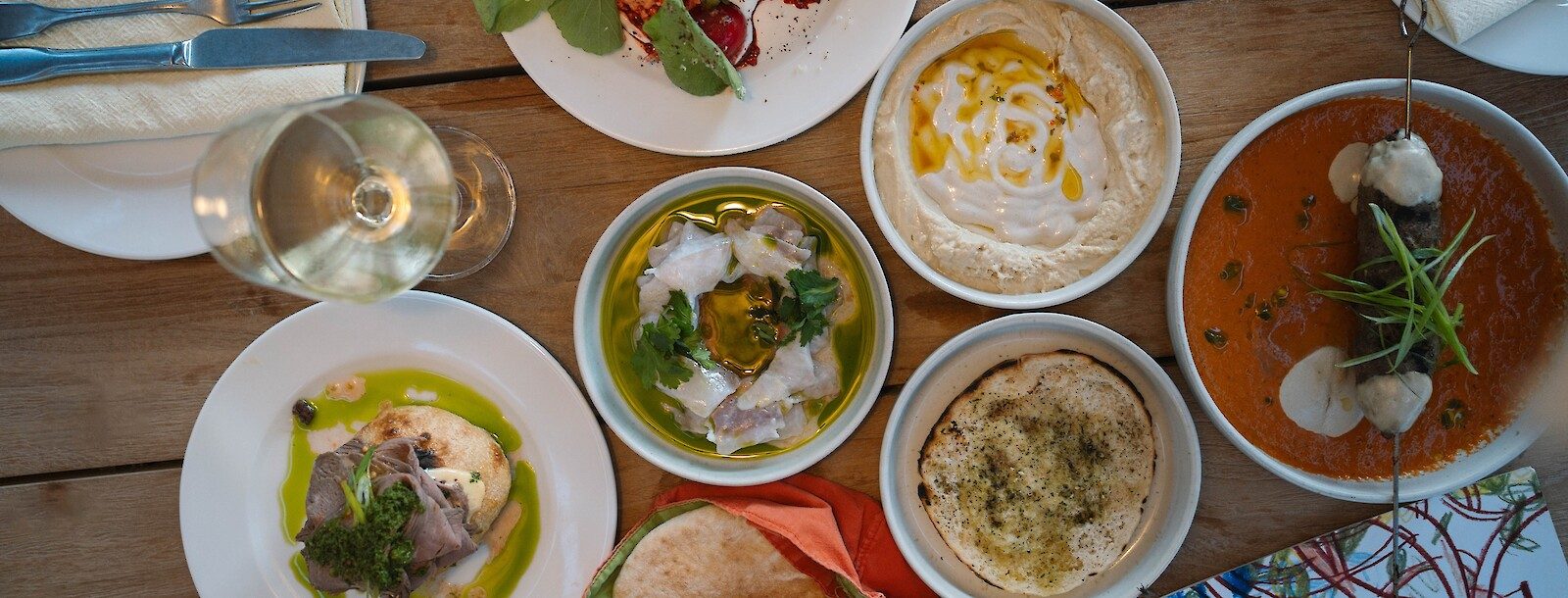 Overhead spread of mezze-style small plates, hummus, and a glass of white wine at NENI restaurant inside Bikini Island & Mountain Hotel Es Trenc