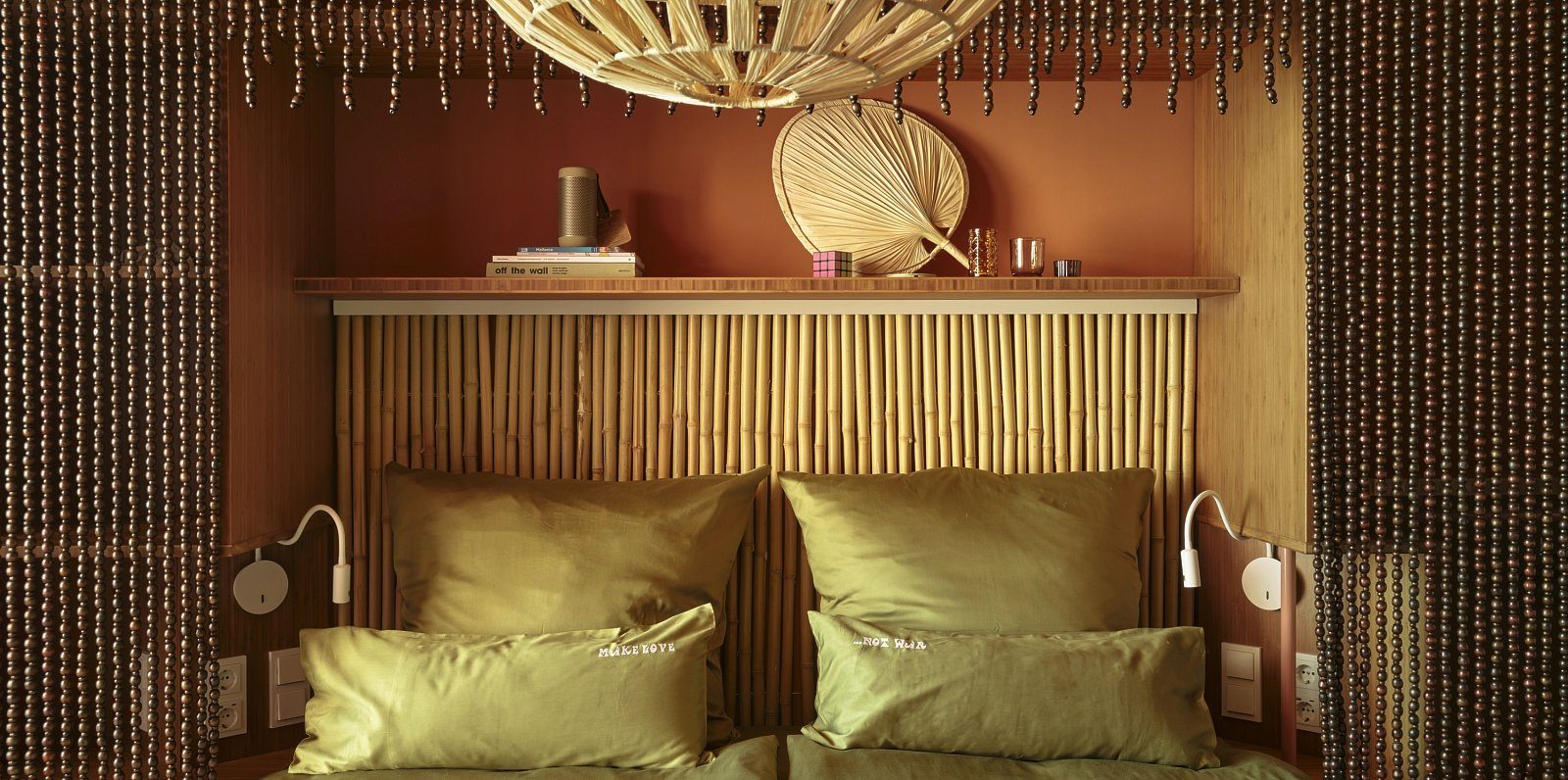 Guest room headboard at Bikini Island & Mountain Hotel Es Trenc with a woven bamboo wall, beaded curtain, and olive-green silk pillows