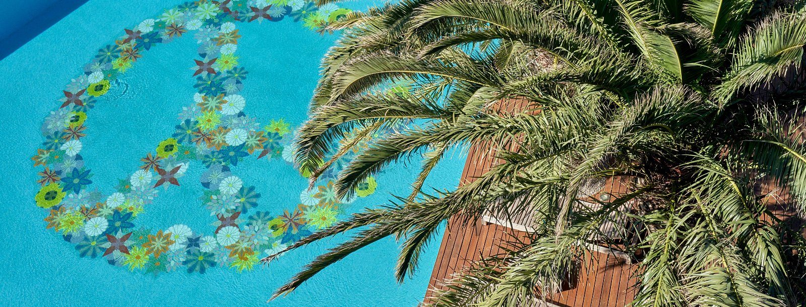 Pool floor at Bikini Island & Mountain with a mosaic floral peace-sign design in turquoise water, palm fronds overhanging the wood deck