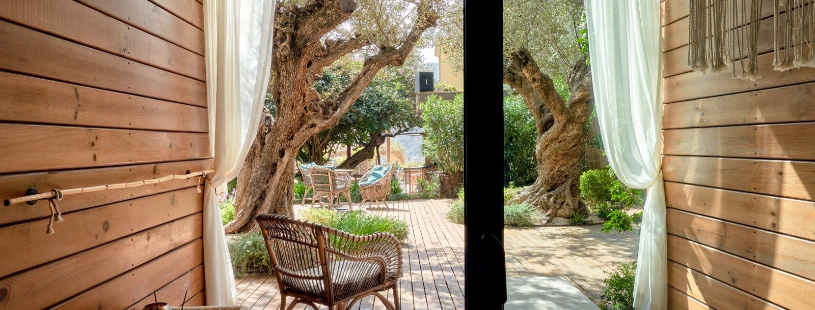 Private room terrace at Bikini Island & Mountain with wood-clad walls, sheer curtains and a wicker chair on a wood deck among old olive trees
