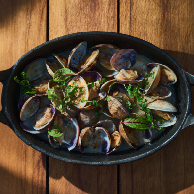 A cast-iron dish of clams scattered with chopped herbs, shot from above on a wooden table.