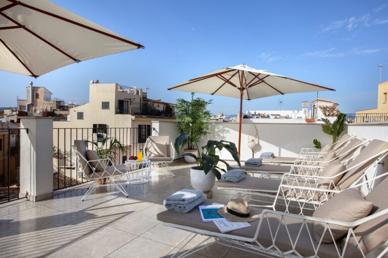 Rooftop terrace at Posada Terra Santa with white and terracotta umbrellas, wicker loungers and potted palms over the rooftops of Palma's old town
