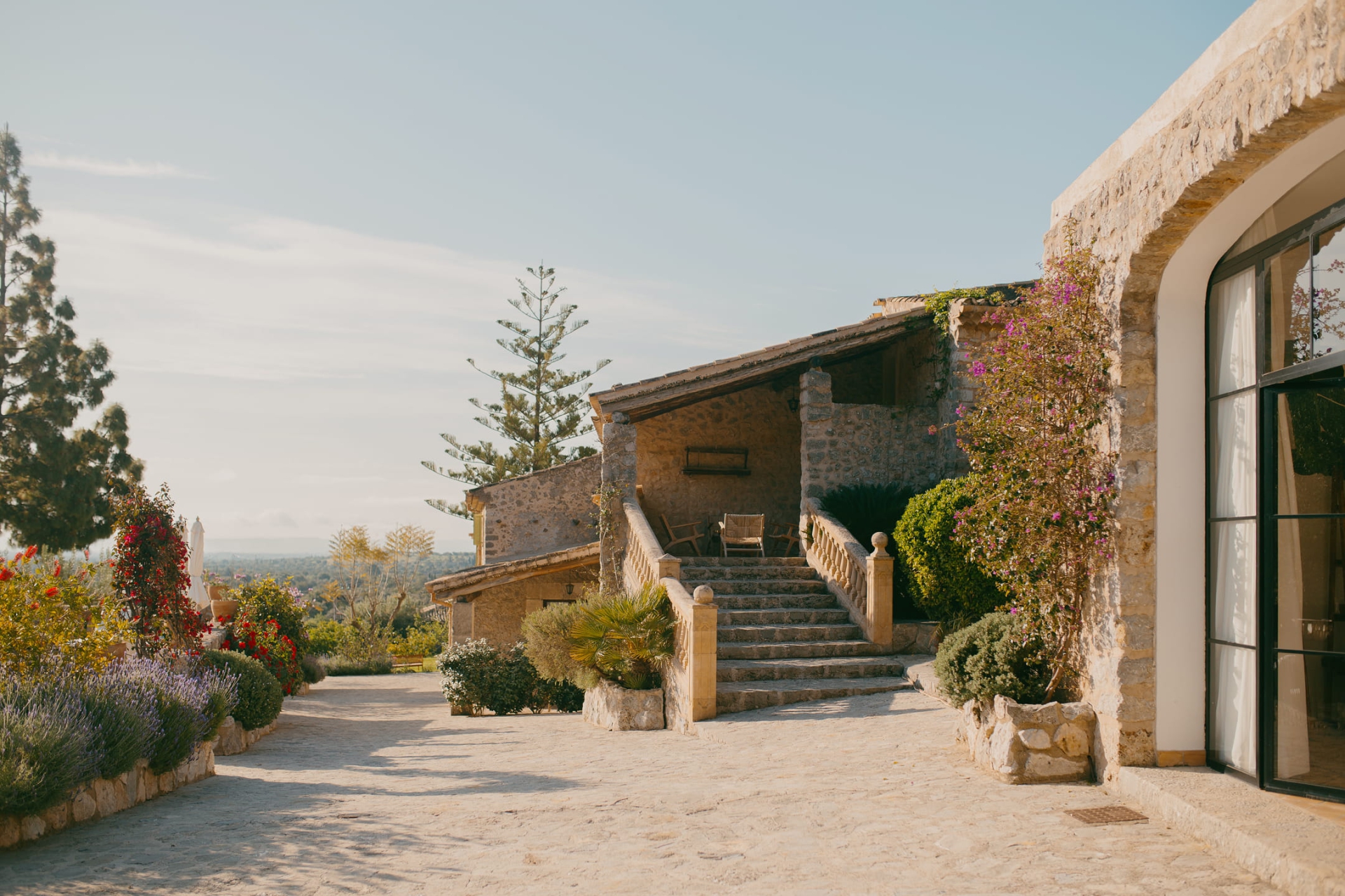 The estate's stone buildings with a balustraded staircase, bougainvillea over the wall and a gravel courtyard