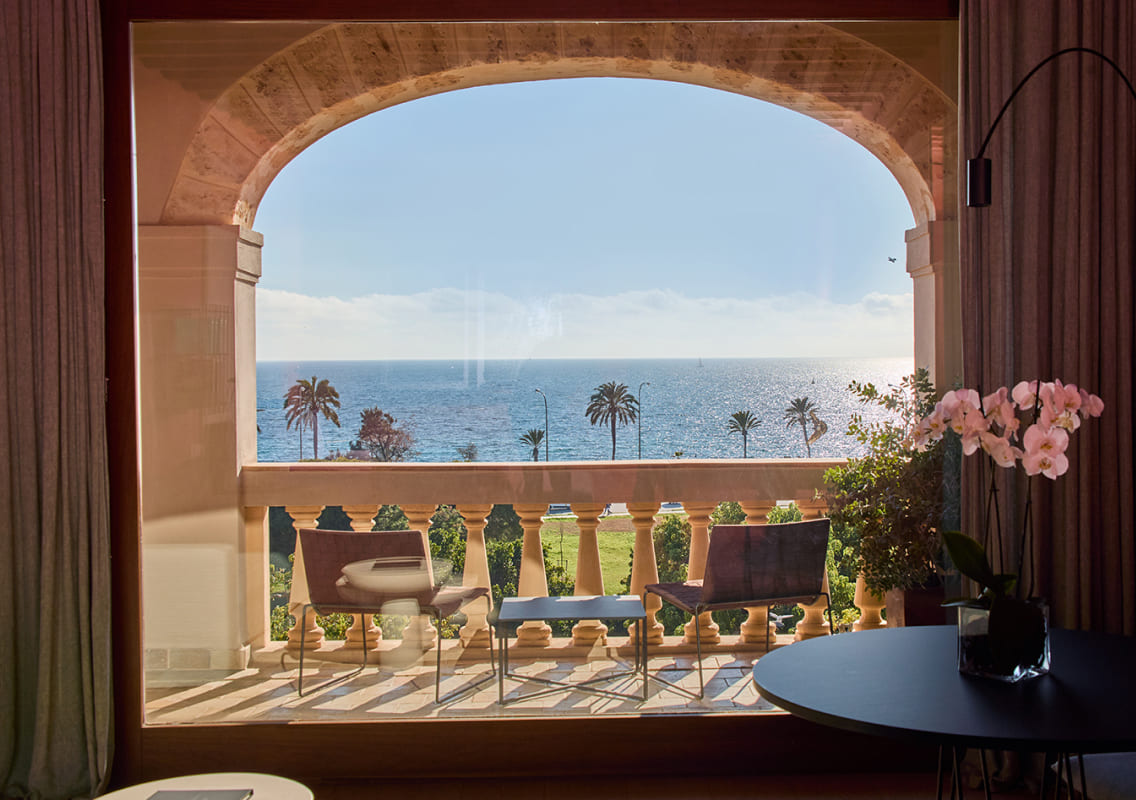 Stone arch framing a balustraded balcony with palm trees and the sea beyond