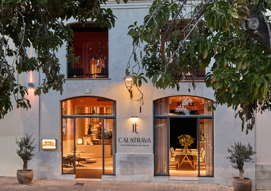 Street-level entrance of the hotel with two arched glass doors, olive trees in pots and the Calatrava sign