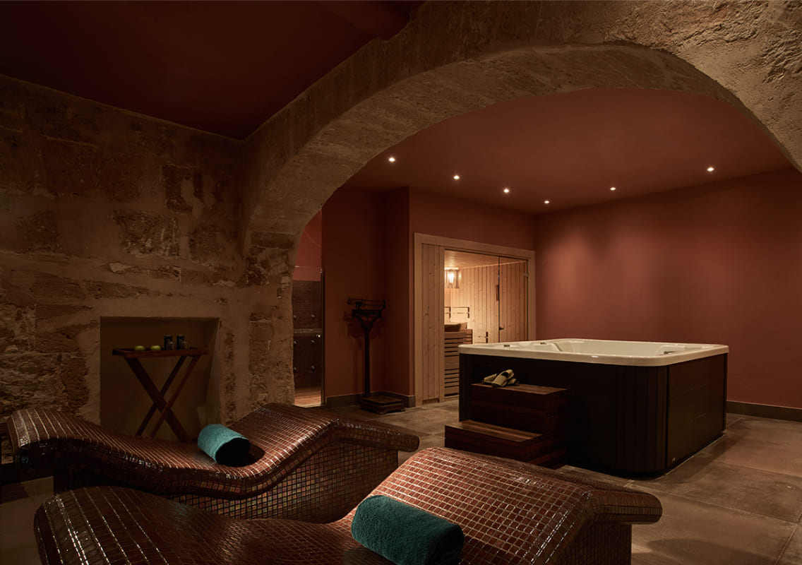 Stone-vaulted spa room with a jacuzzi and woven thermal loungers
