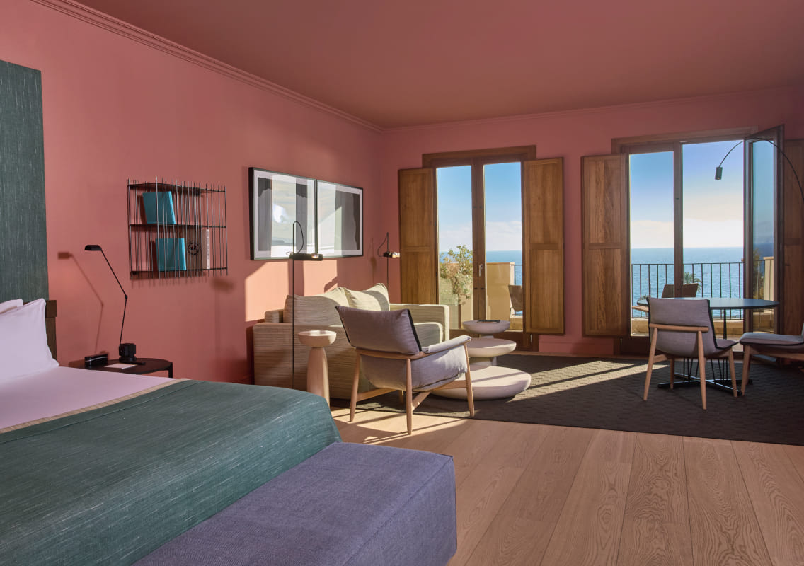 Terracotta-walled suite bedroom with a seating area and shuttered doors opening to a sea view