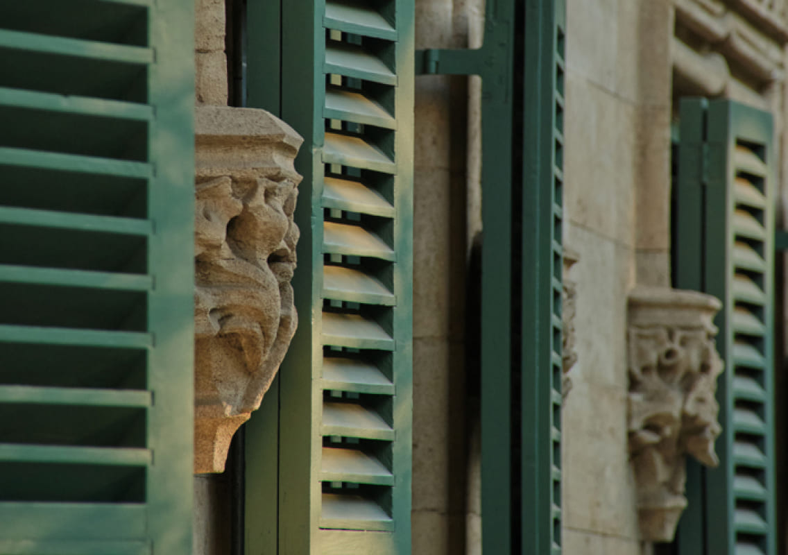 Carved stone facade detail with green shutters at Can Alomar