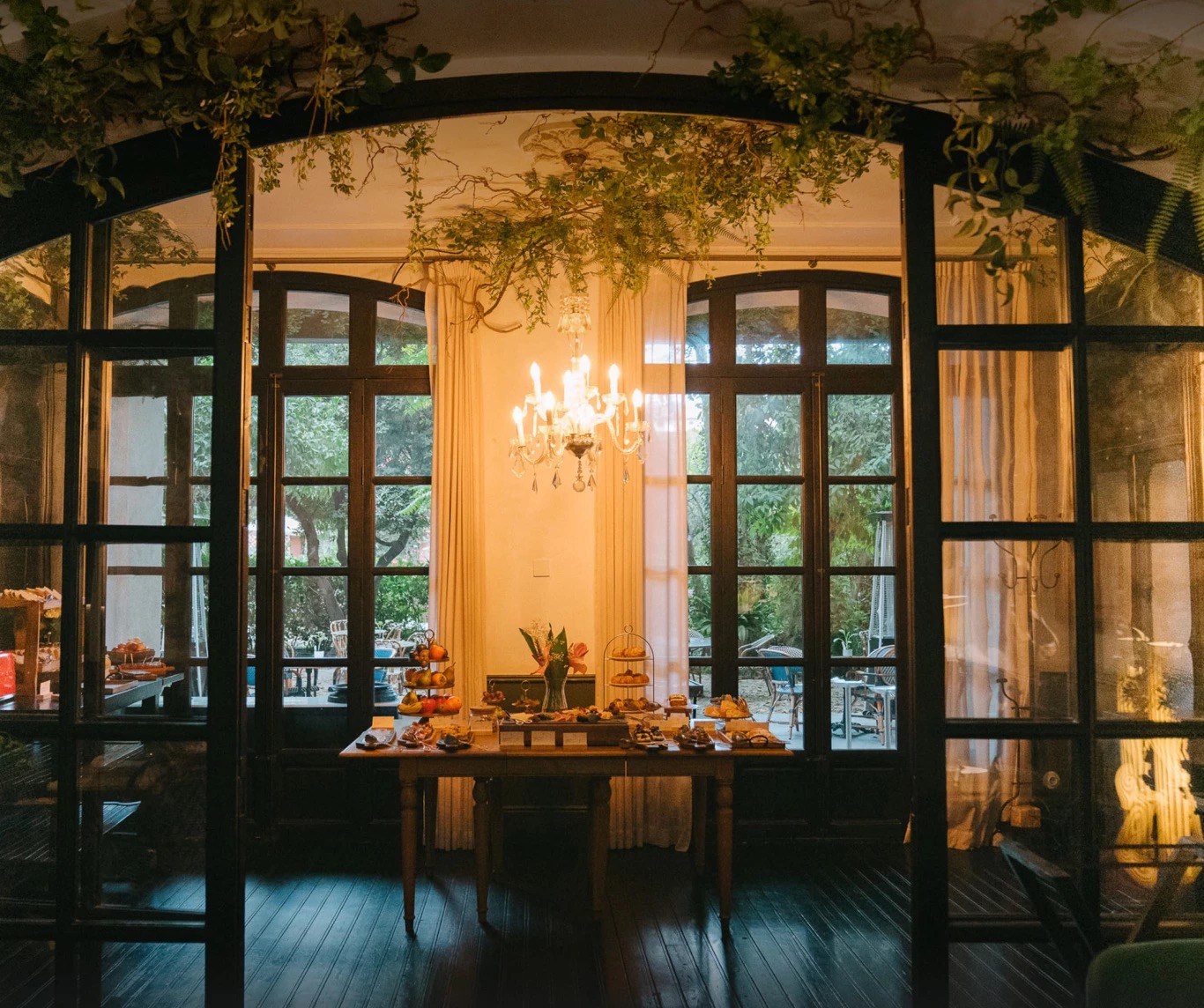 Breakfast spread on a table beneath a chandelier, glass doors open to the garden