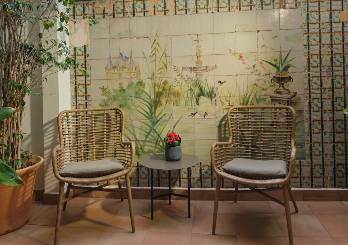 Rattan armchairs on a tiled terrace in front of a painted ceramic mural