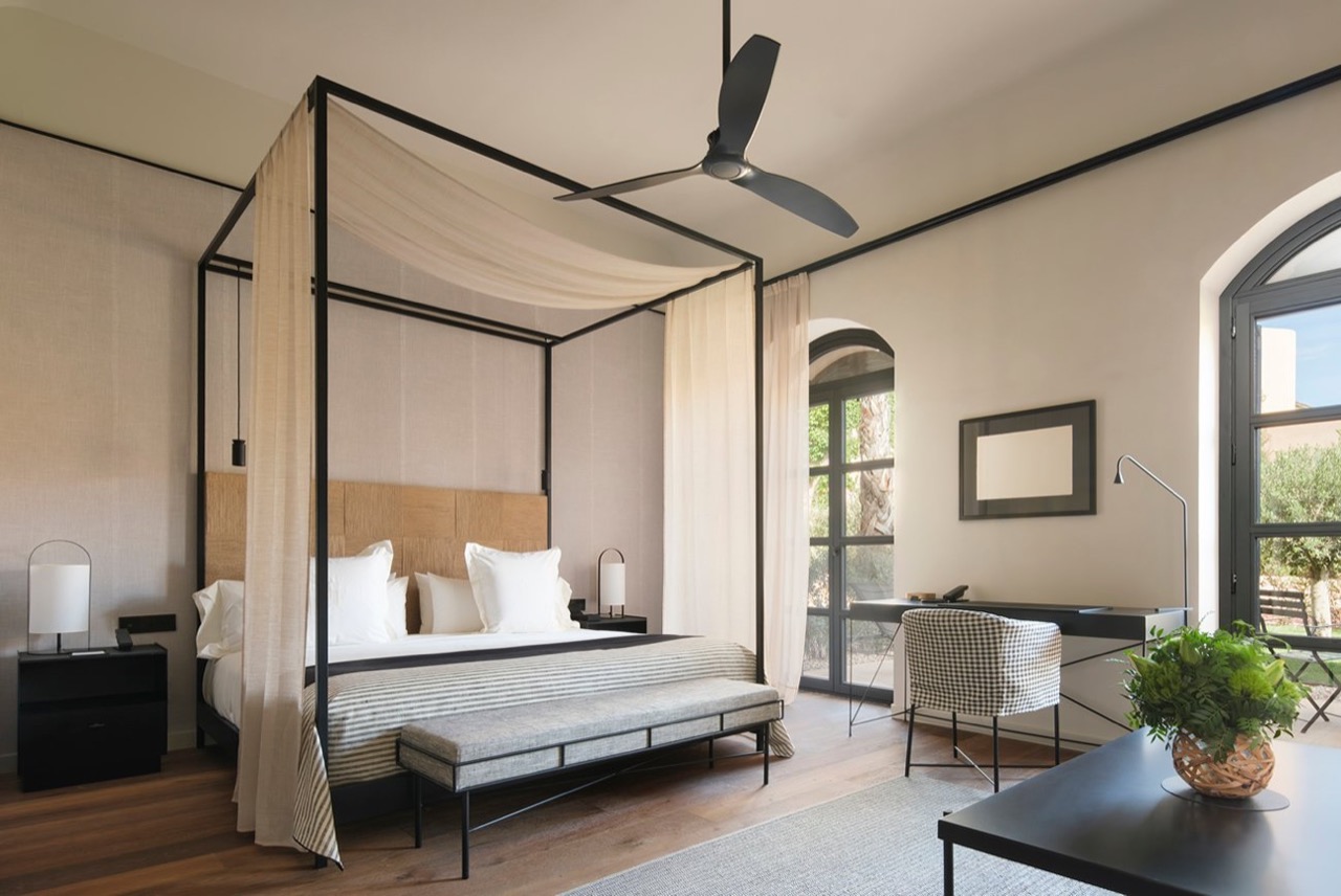 Suite at Can Ferrereta with a black four poster bed, sheer curtains, and a desk by an arched window