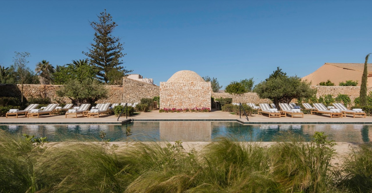 Outdoor pool at Can Ferrereta lined with striped sun loungers, framed by a stone dome structure and gardens