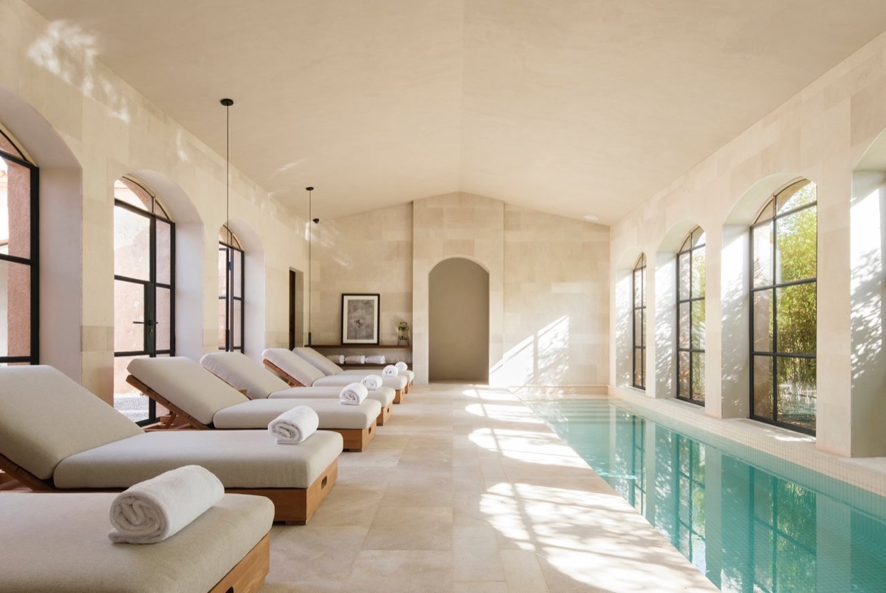 Indoor heated pool at Can Ferrereta's SA CALMA spa, with sun loungers along stone arched windows