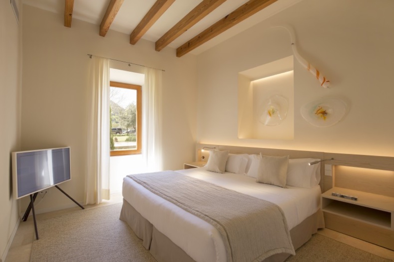 Bedroom at Can Simoneta with exposed wood beam ceiling and a window looking onto the grounds