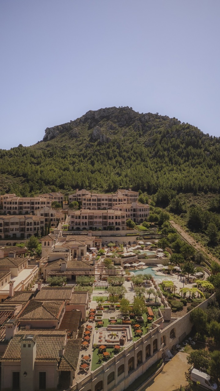 Aerial view of Cap Vermell Grand Hotel's buildings, pool area, and gardens set against the Canyamel mountains
