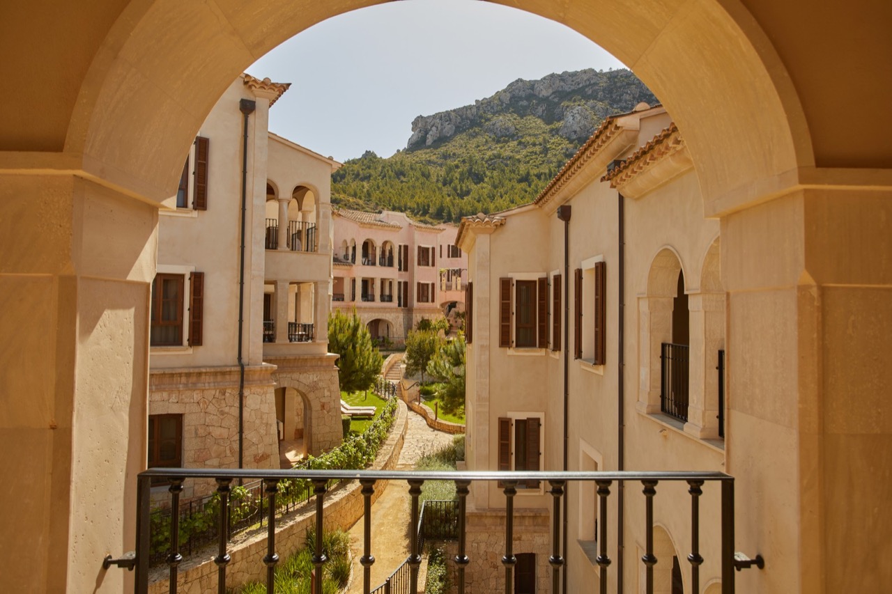 Stone archway framing a view of Cap Vermell Grand Hotel's courtyard, gardens, and the mountains behind