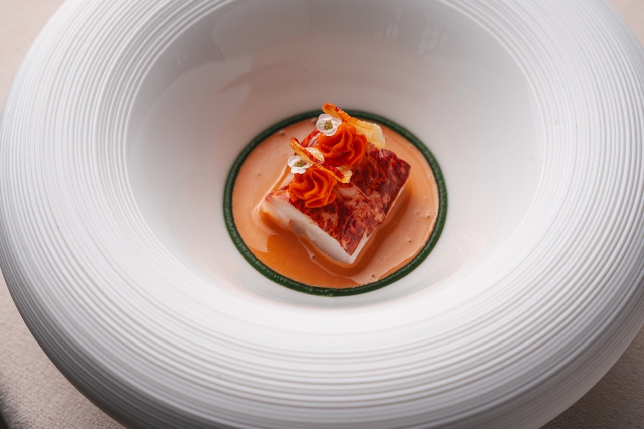 Plated fish dish with sauce and edible flowers served on a textured white bowl at the hotel's restaurant
