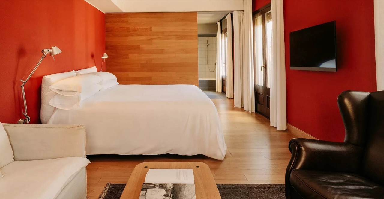 Corner suite bedroom with a red accent wall, wood panelling, a white bed, leather armchair and a glimpse of the bathroom at Casa Camper Barcelona.