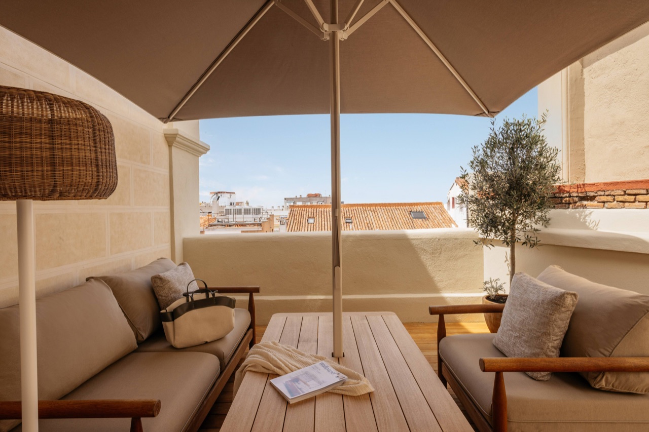 Covered rooftop terrace with a large umbrella, outdoor sofas, a potted olive tree and a view over Madrid's tiled rooftops.