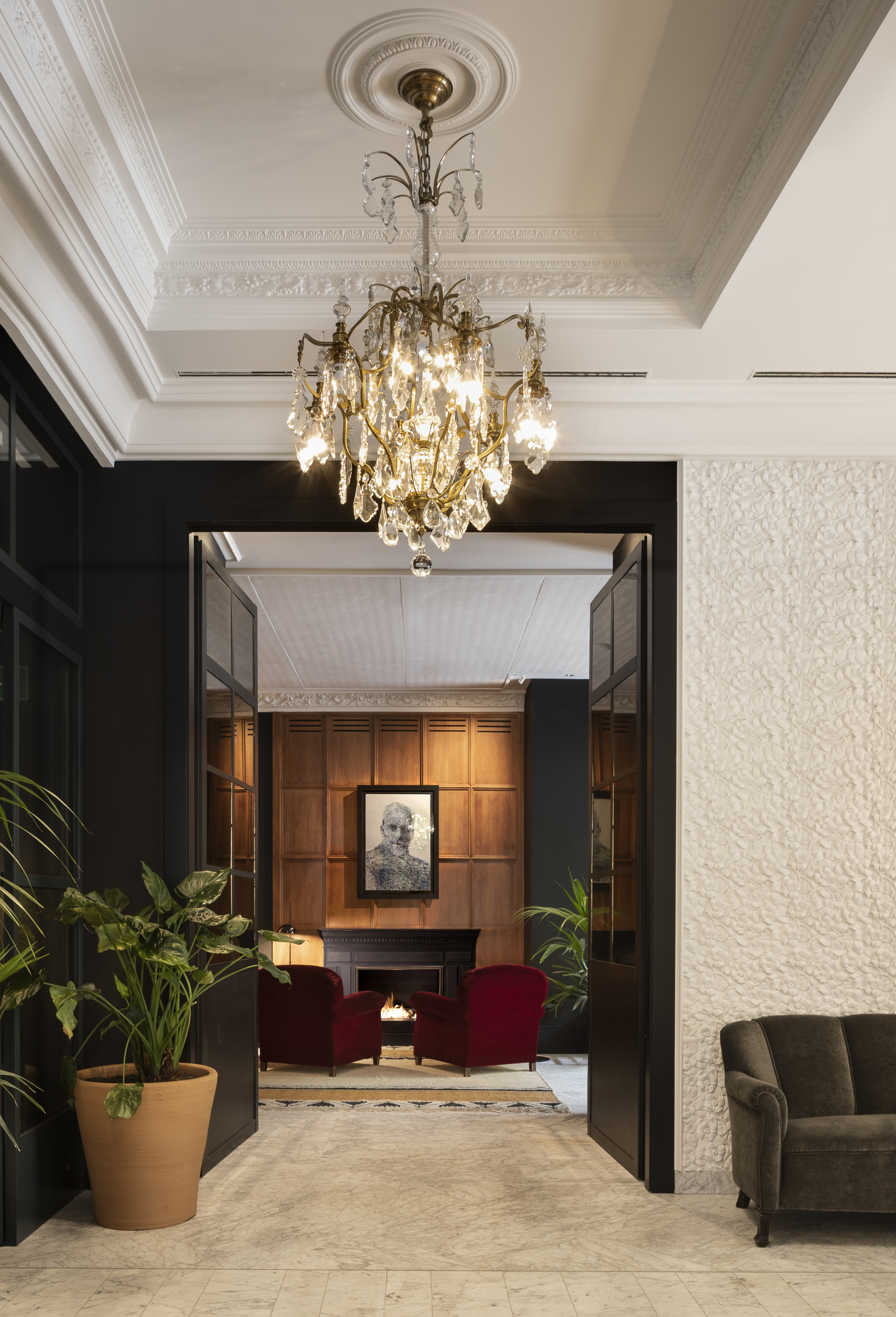 Lounge with a crystal chandelier, a fireplace and red velvet armchairs