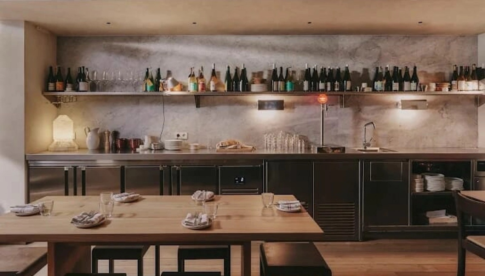 Arraval restaurant open-kitchen counter with wine bottles and set tables