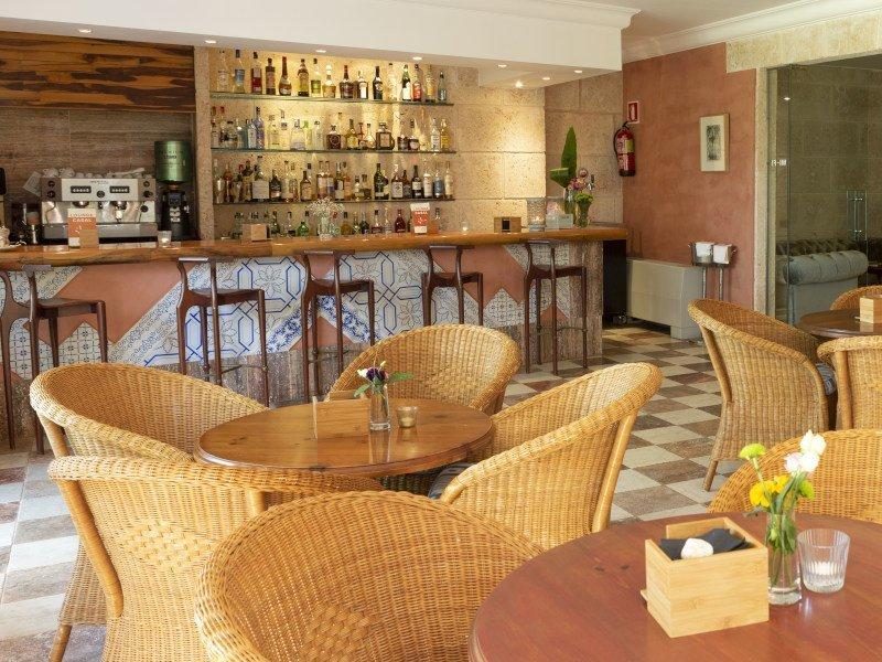 Hotel bar at Casal Santa Eulalia with a tiled counter, shelves of spirits, an espresso machine, and wicker chairs around dark wood tables